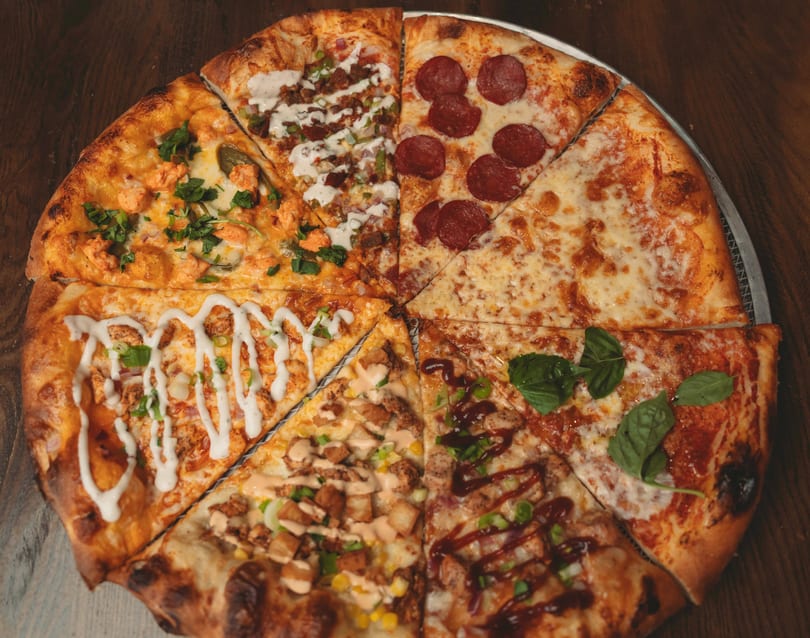 A whole pizza cut into eight slices, each with a unique topping combination.