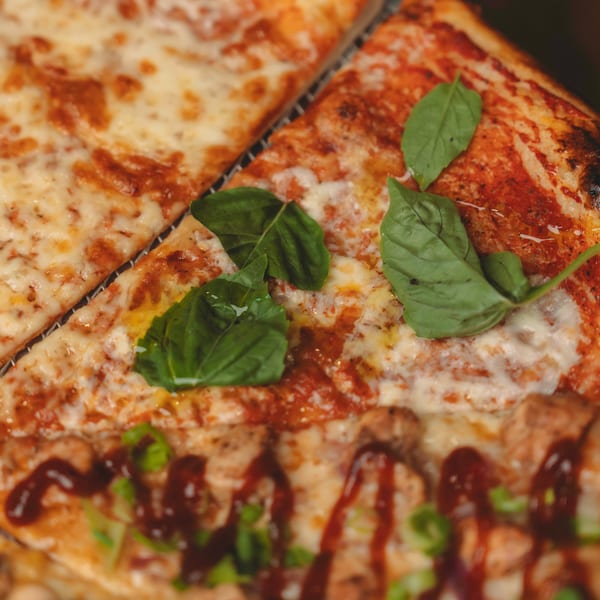 Close-up of three pizza slices with different toppings, including cheese, basil, and BBQ sauce.