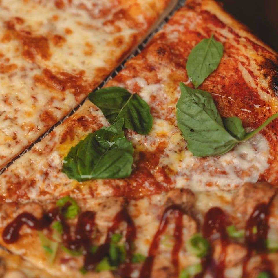 Close-up of three pizza slices with different toppings, including cheese, basil, and BBQ sauce.