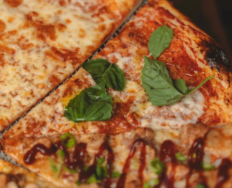 Close-up of three pizza slices with different toppings, including cheese, basil, and BBQ sauce.
